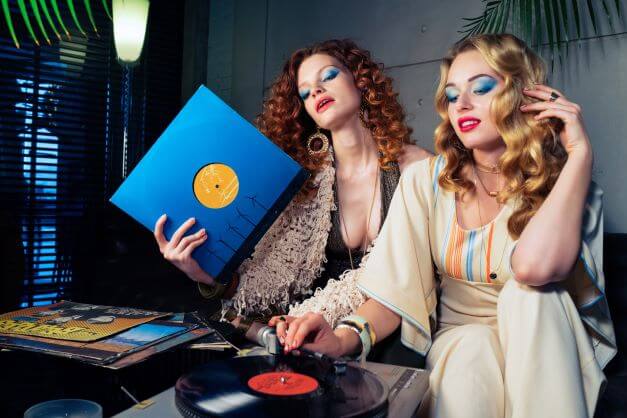 two girls in 70's fashion pieces listening to record player