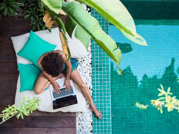 A nomad worker uses laptop by a pool